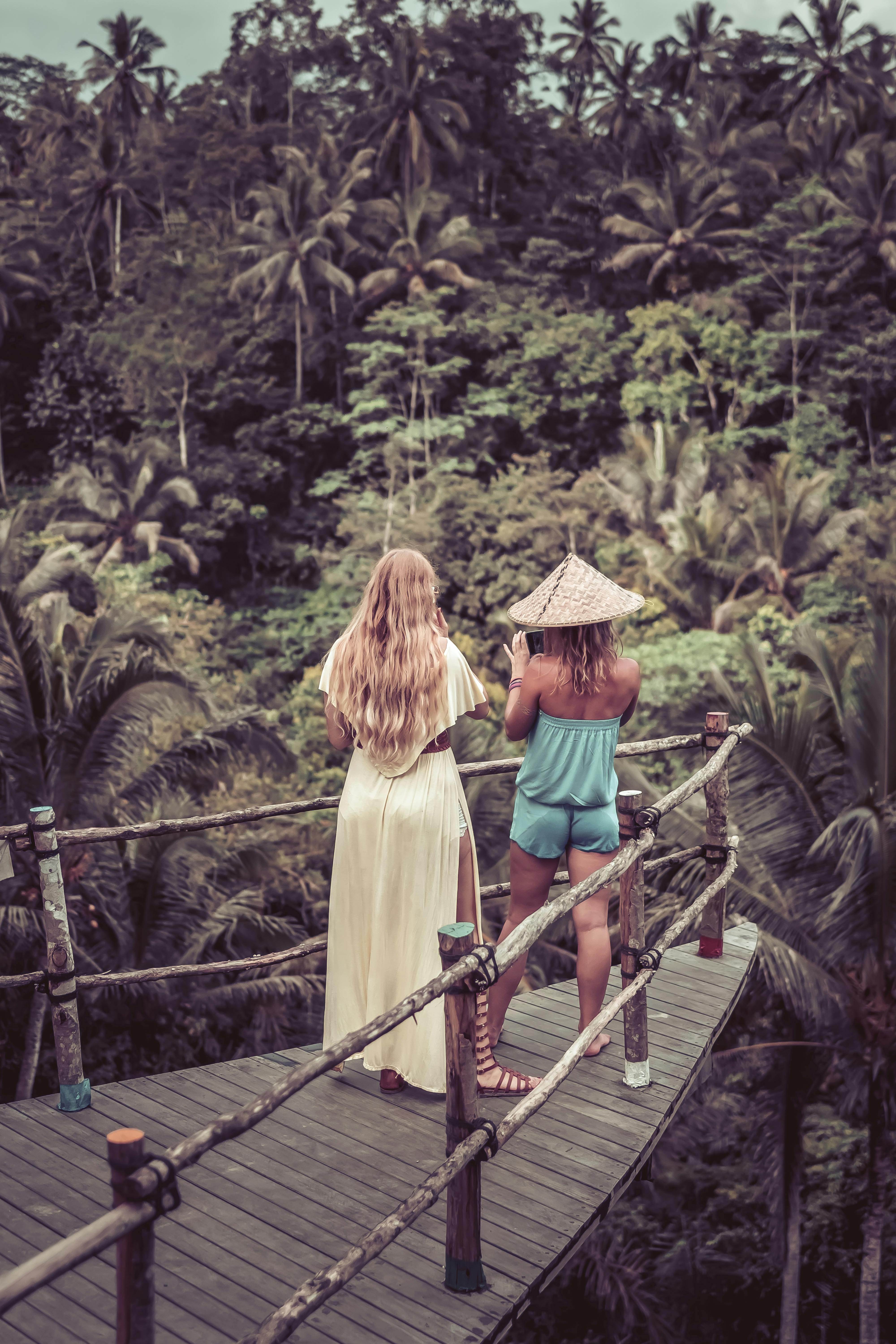 two woman standing beside railing looking in forest