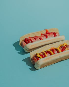 Two tasty hot dogs topped with ketchup and mustard on a light blue background.