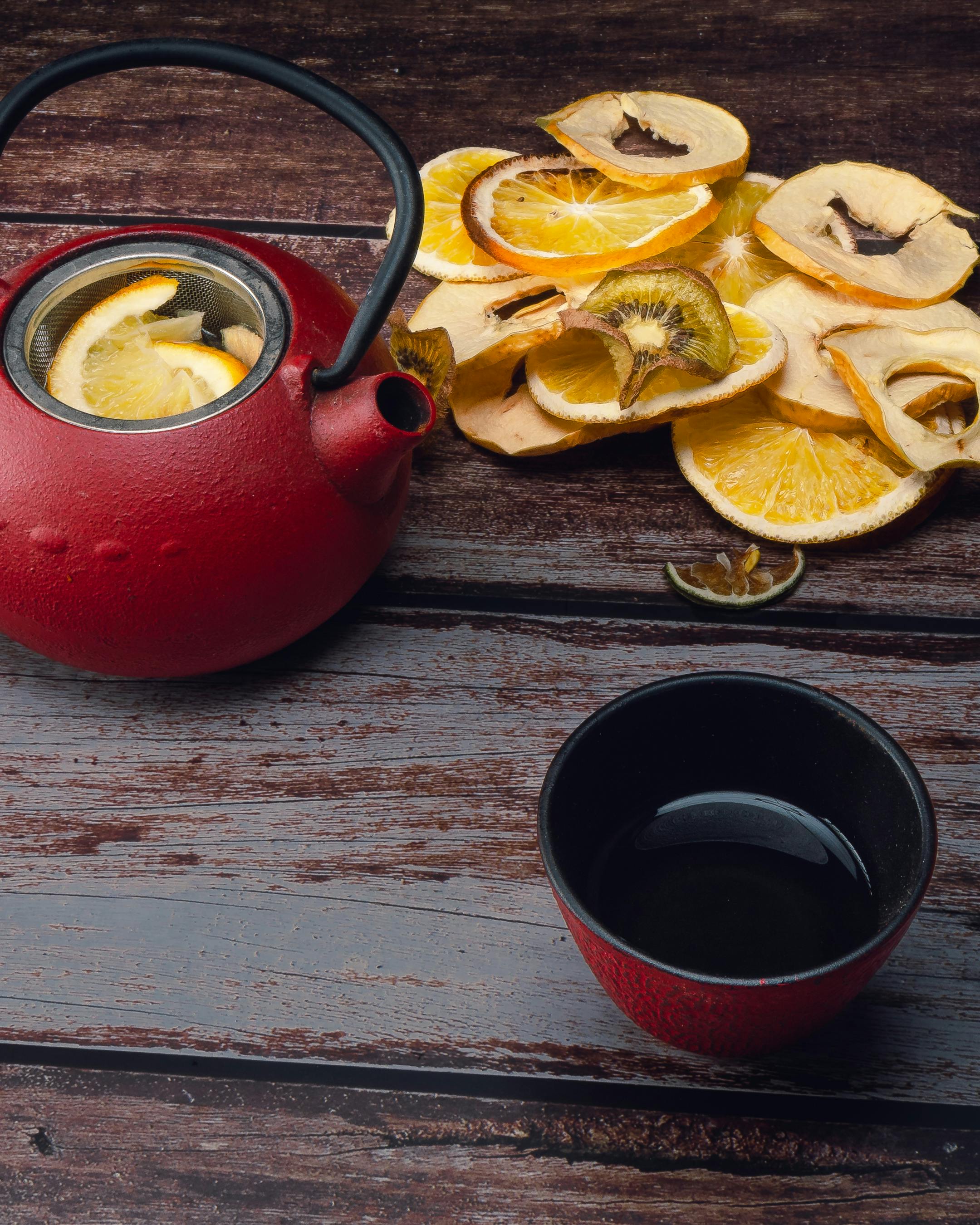 Red teapot and cup with dried citrus slices on wooden surface.