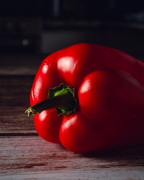 Free A vibrant red bell pepper on a rustic wooden table, showcasing its fresh texture and vivid color. Stock Photo