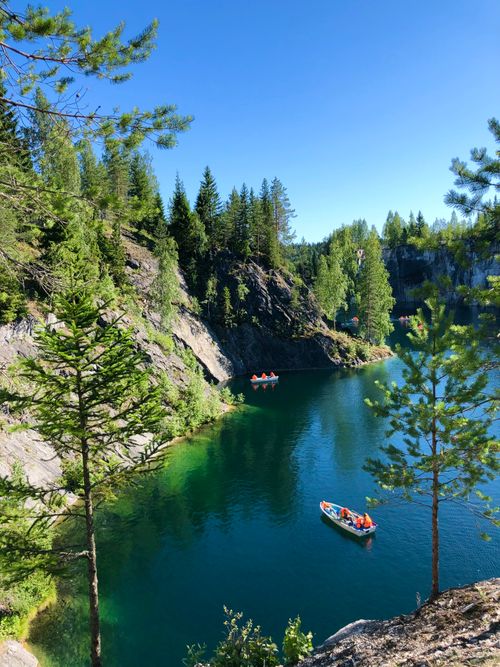 Free Serene lake with boats surrounded by lush forest and rocky cliffs under a clear sky. Stock Photo