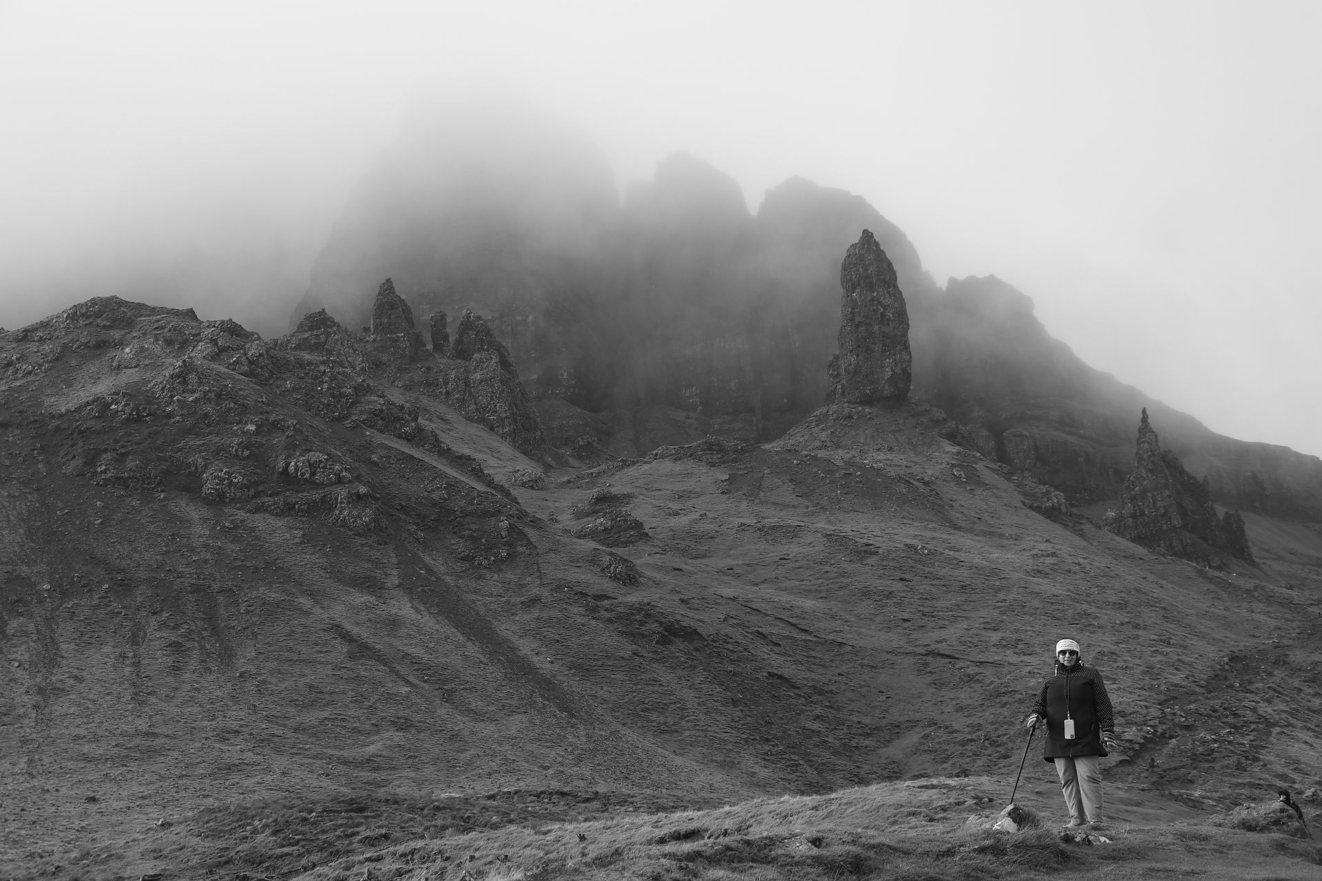 Hiker with hiking poles exploring the misty Old Man of Storr, Scotland's iconic rock formation.