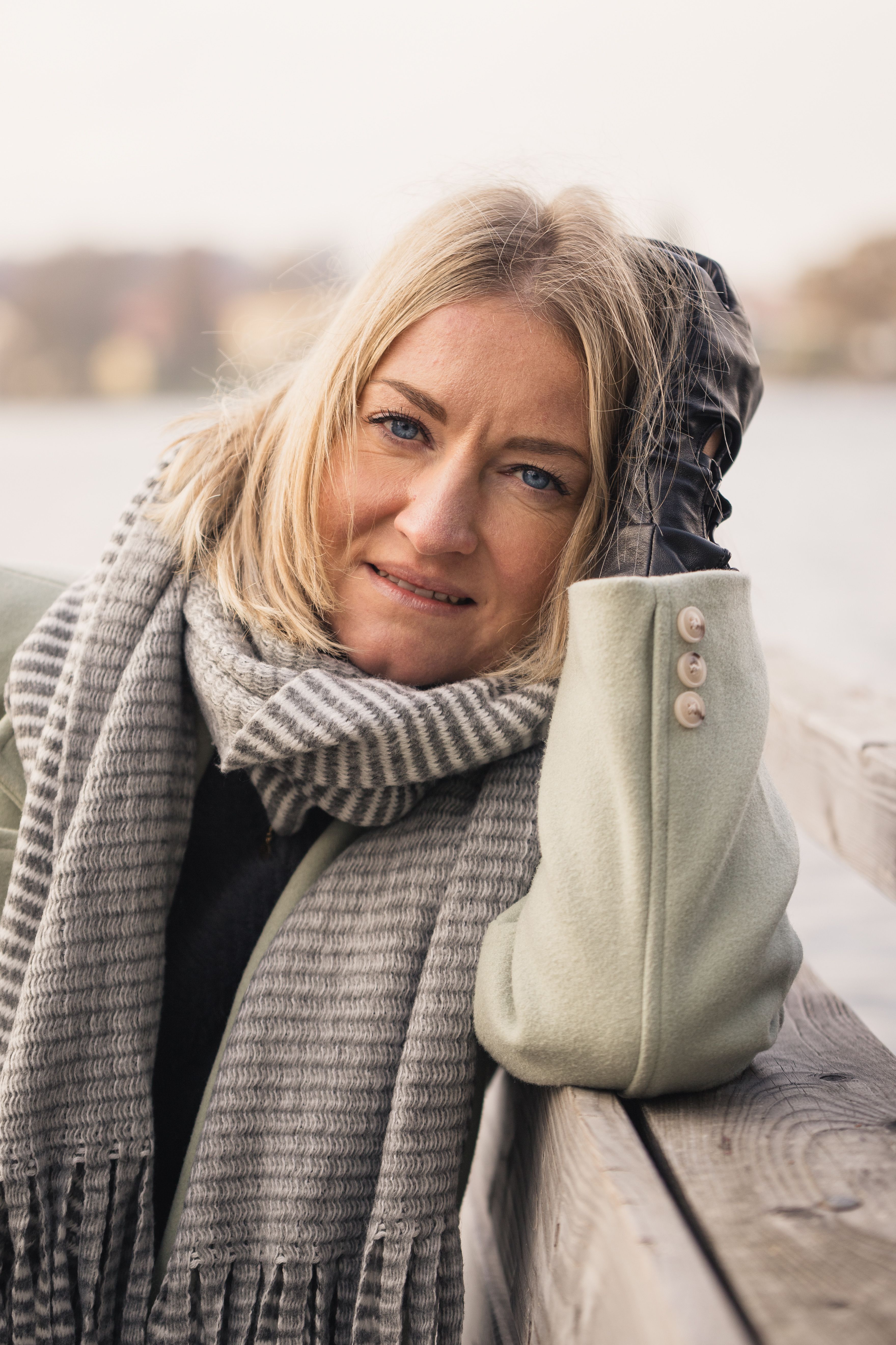 Elegant woman posing by a lake in Weßling, Germany, wrapped in a cozy scarf.