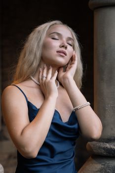 Serene woman posing in navy dress and pearls, exuding elegance.