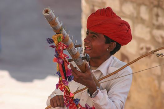 A Rajasthani musician plays a colorful traditional instrument outdoors.