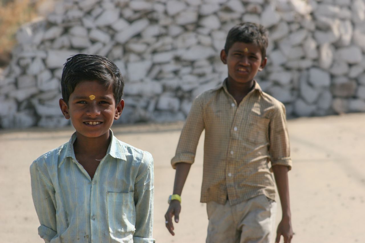 two boys outdoors one smiling against a pile of white stones on a sunn