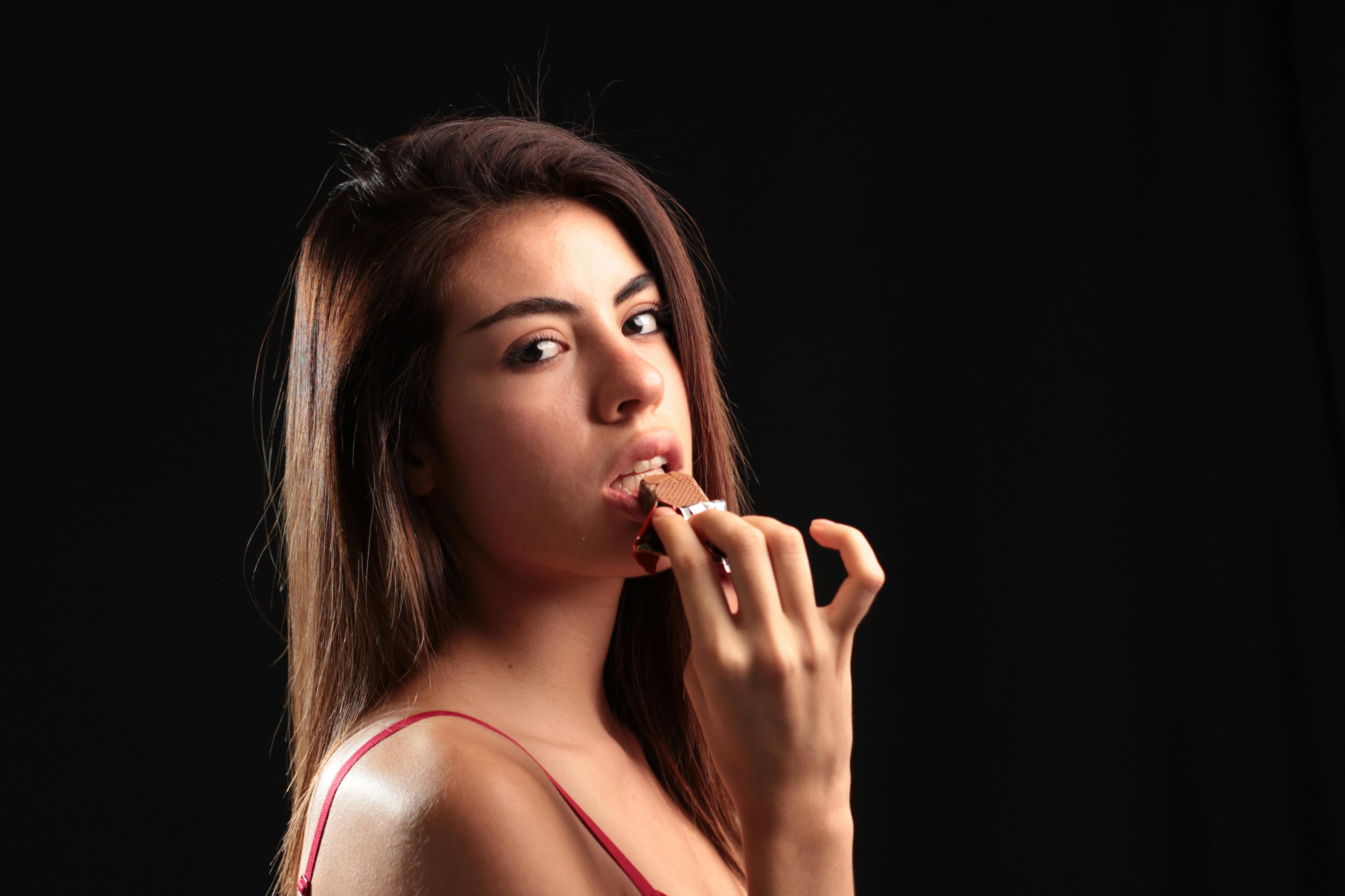 Young woman savoring chocolate in a lively studio atmosphere. Perfect for lifestyle and food concepts.