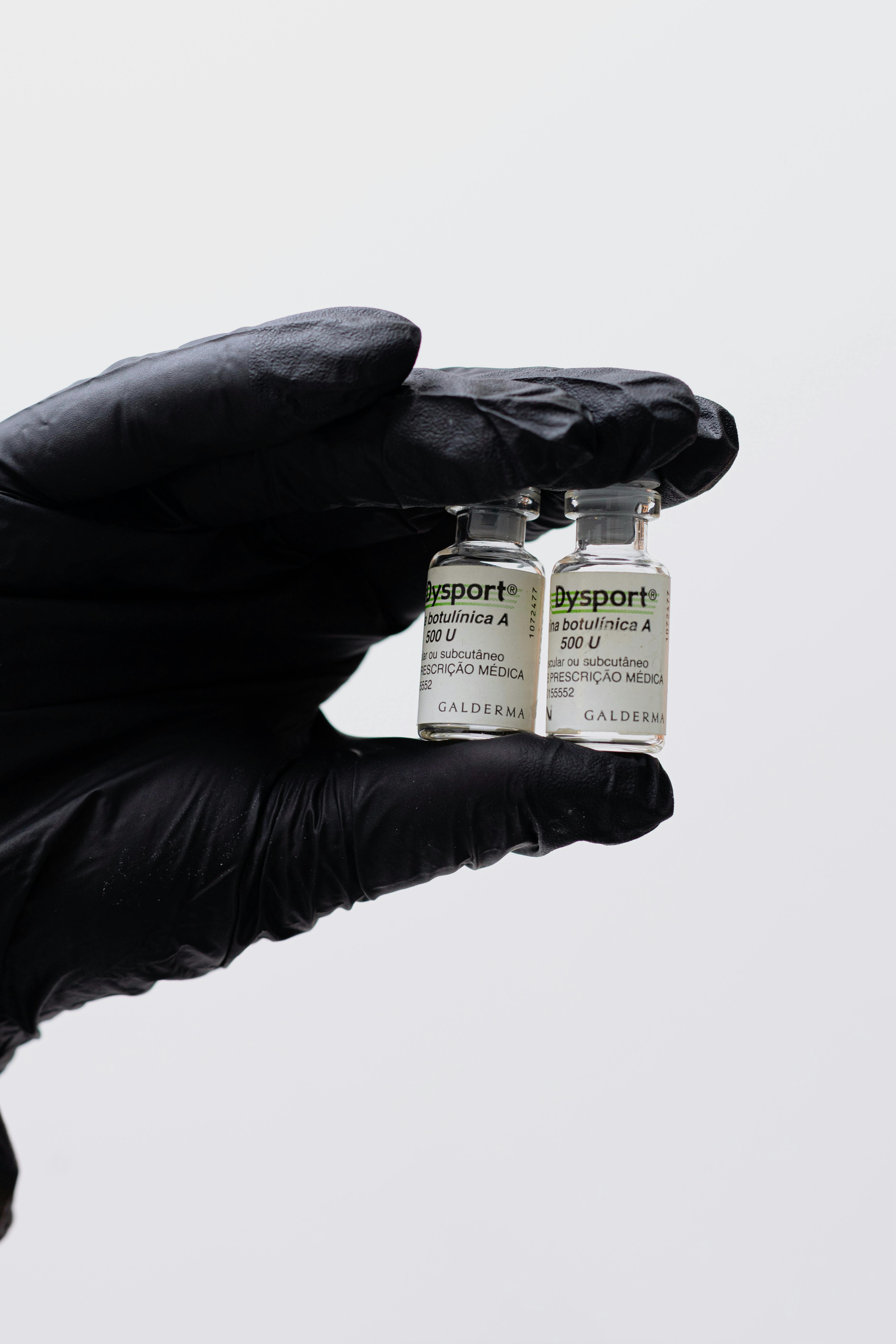 Close-up image of a gloved hand holding two Dysport botulinum toxin vials.