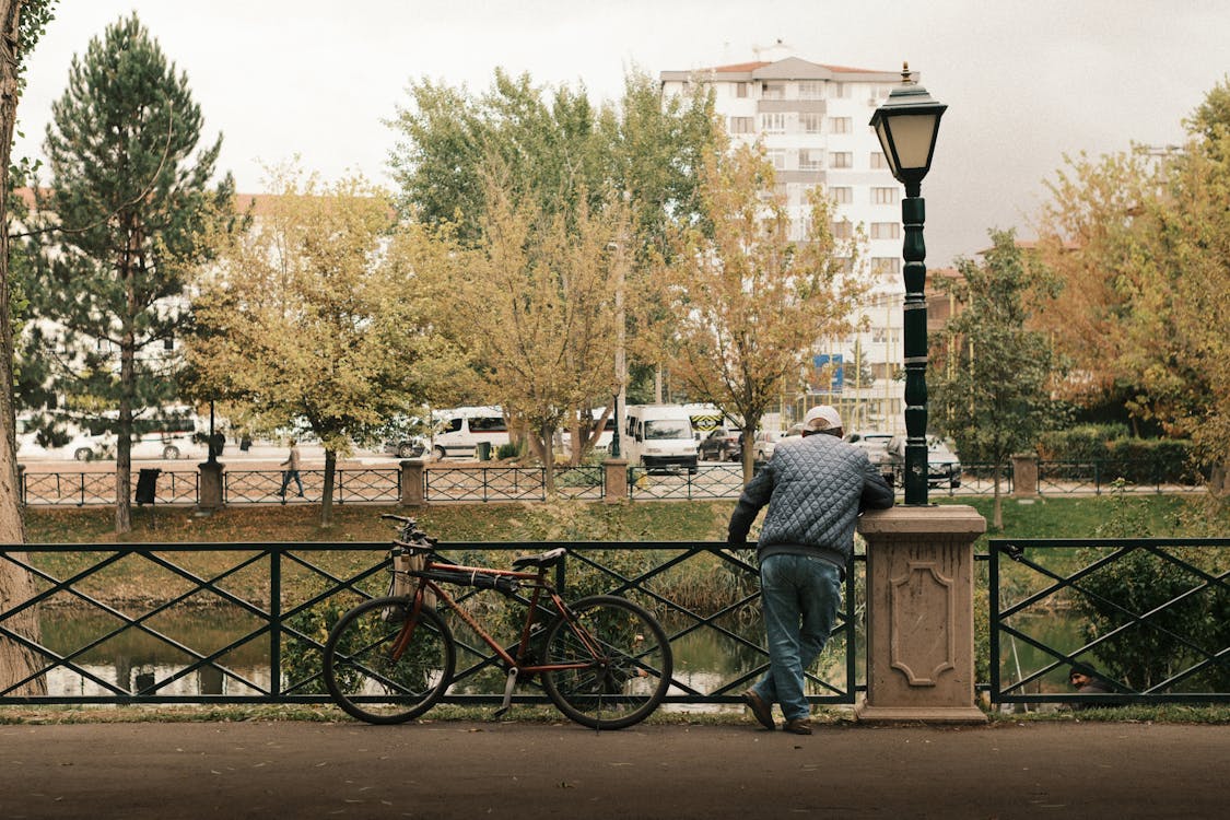 A solitary man stands on an Eskisehir street, holding a bicycle, surrounded by empty urban scenery.