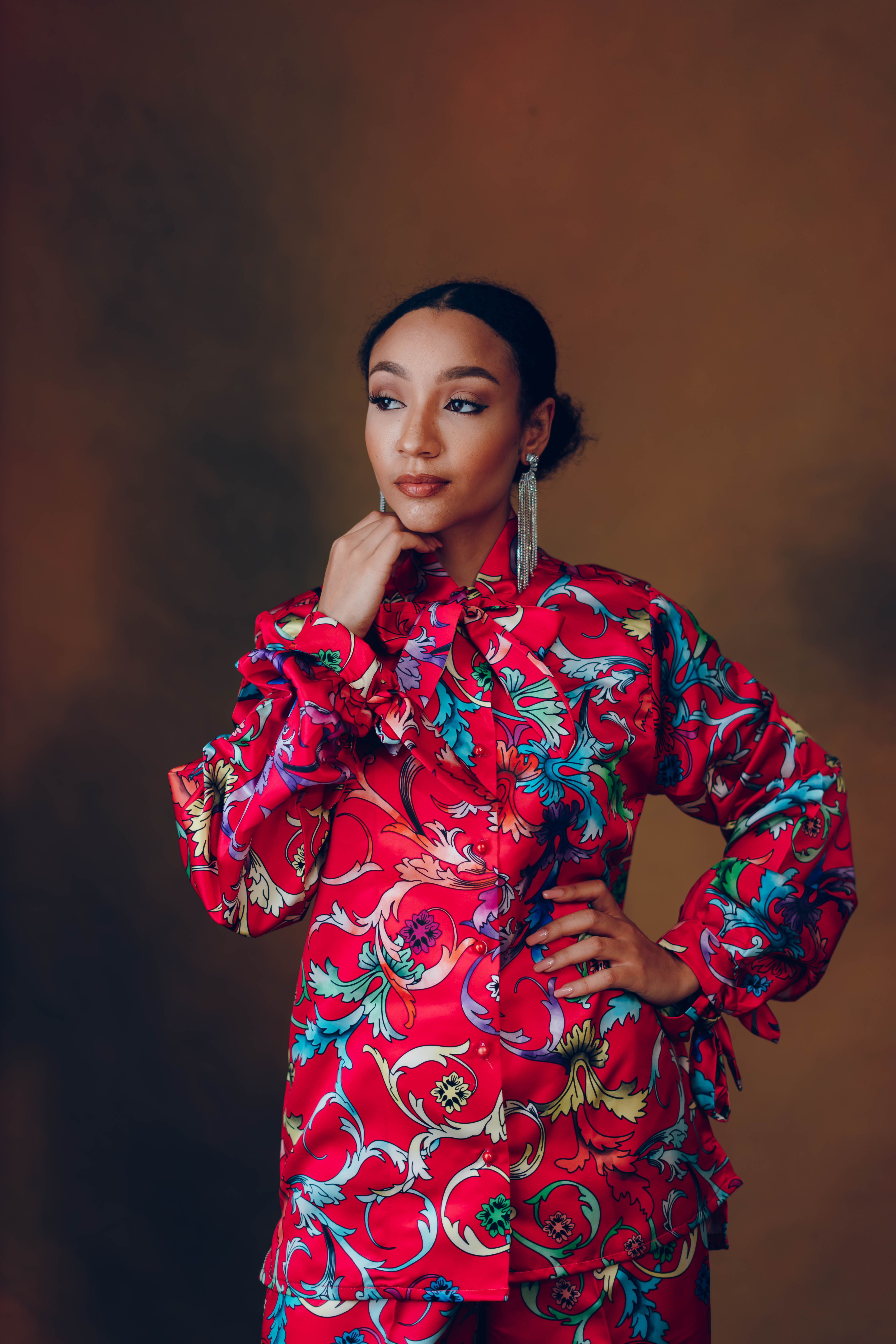 Elegant woman in a vibrant floral outfit poses against a warm background.