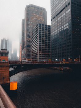 Urban cityscape featuring towering skyscrapers and a mist-covered bridge over water.