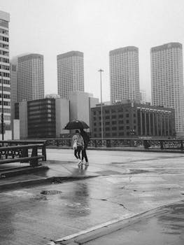A couple walking under an umbrella on a rainy city day with skyscrapers in the background.