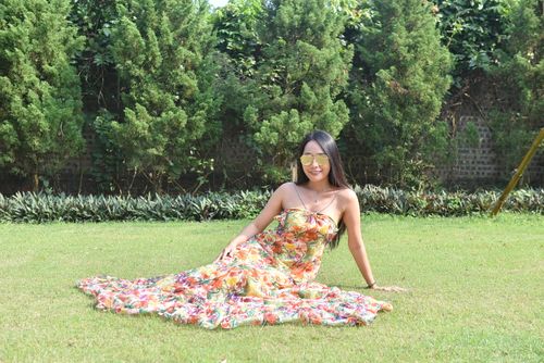 Free A woman enjoys a sunny day outdoors, sitting on green grass in a vibrant floral dress. Stock Photo