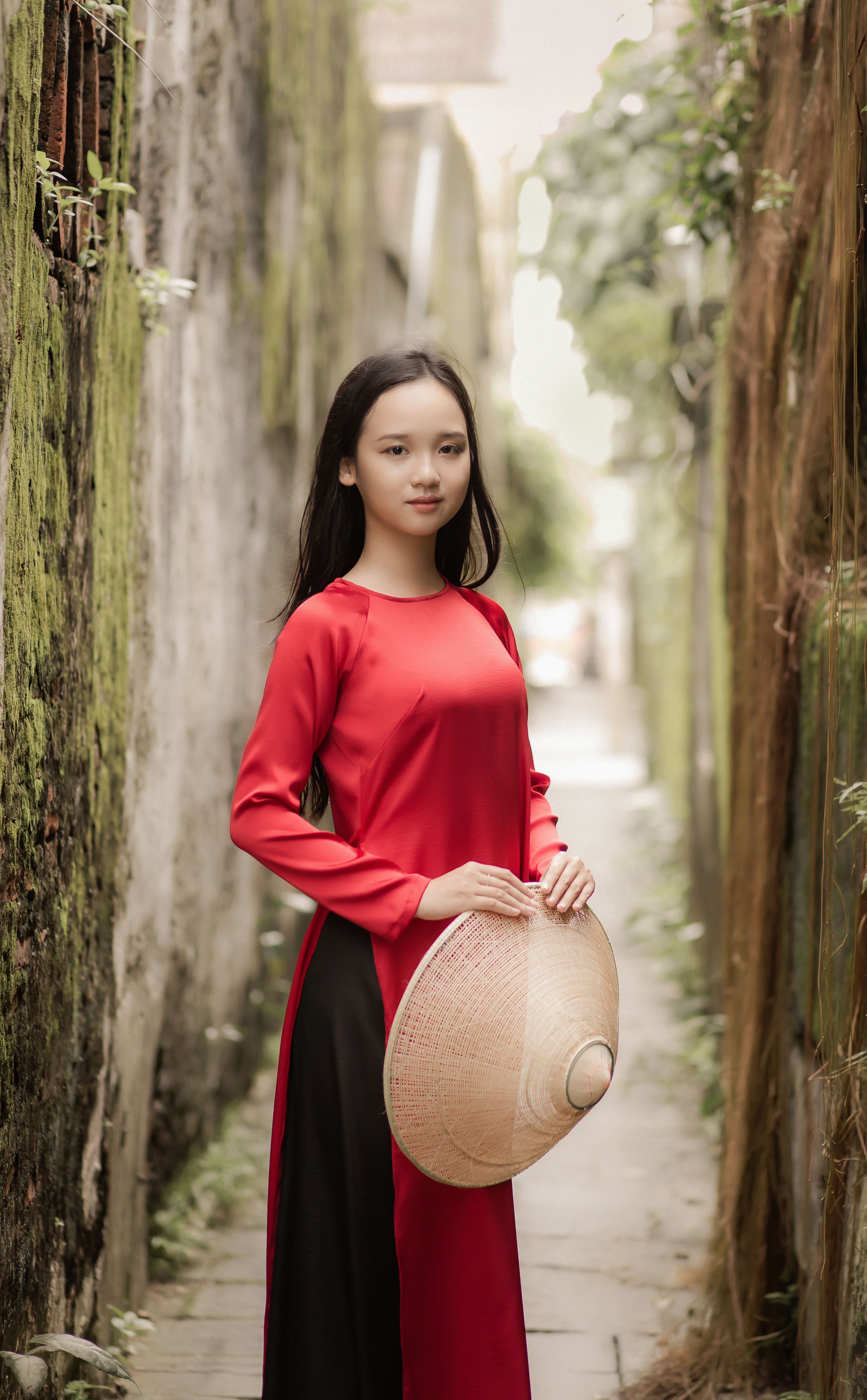 Portrait of a young woman in a red áo dài in Hoi An, Vietnam, showcasing cultural heritage.