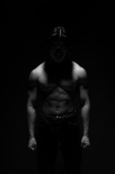 Artistic monochrome portrait of a muscular man in moody lighting.
