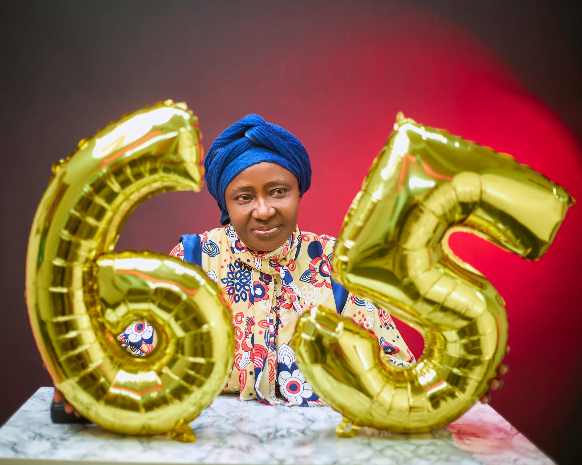 Senior woman celebrating 65th birthday with golden balloons indoors.