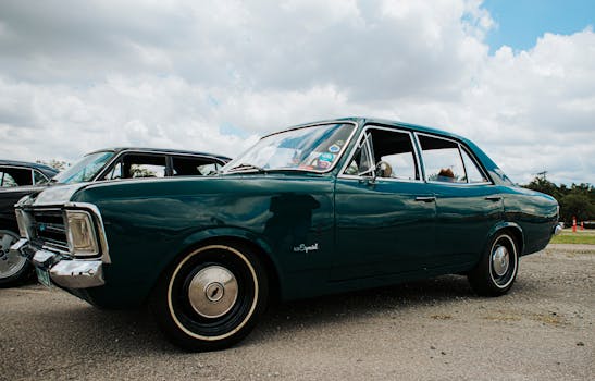 A vintage green car displayed outdoors at a car show on a sunny day.