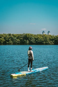 A person paddleboarding on a calm lake with city buildings in the background.