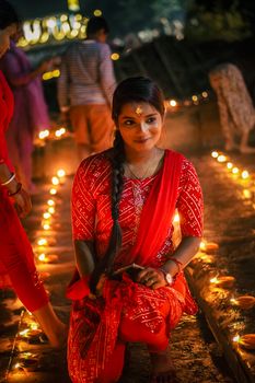 Woman kneeling among oil lamps during a vibrant night festival celebration.