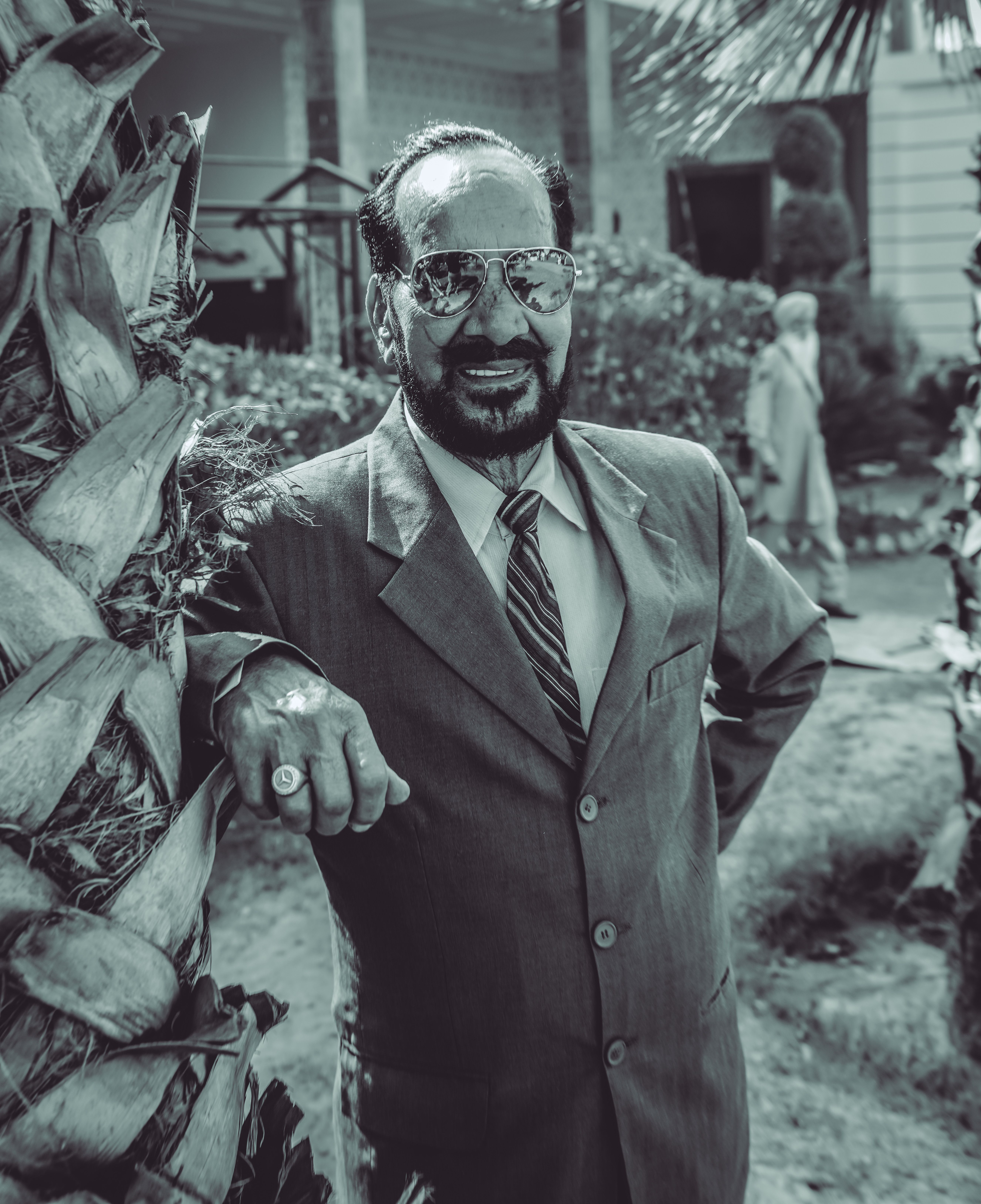 Vintage-style photo of an older man outdoors in a suit by a palm tree.