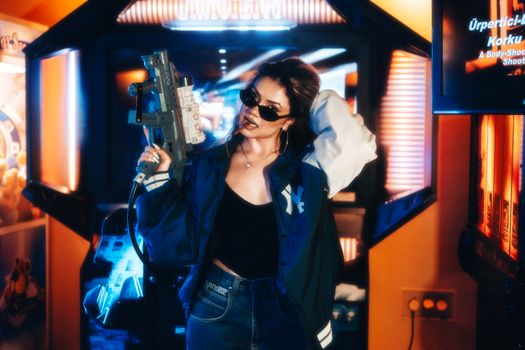 Fashionable young woman in an arcade holding a toy gun enjoying leisure time.
