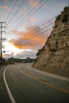 Curving road along a rocky hillside under a vibrant sunset in Malibu, California.