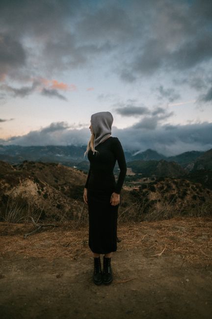 Silhouette of a woman in a hooded outfit gazing over Malibu mountains at dusk.