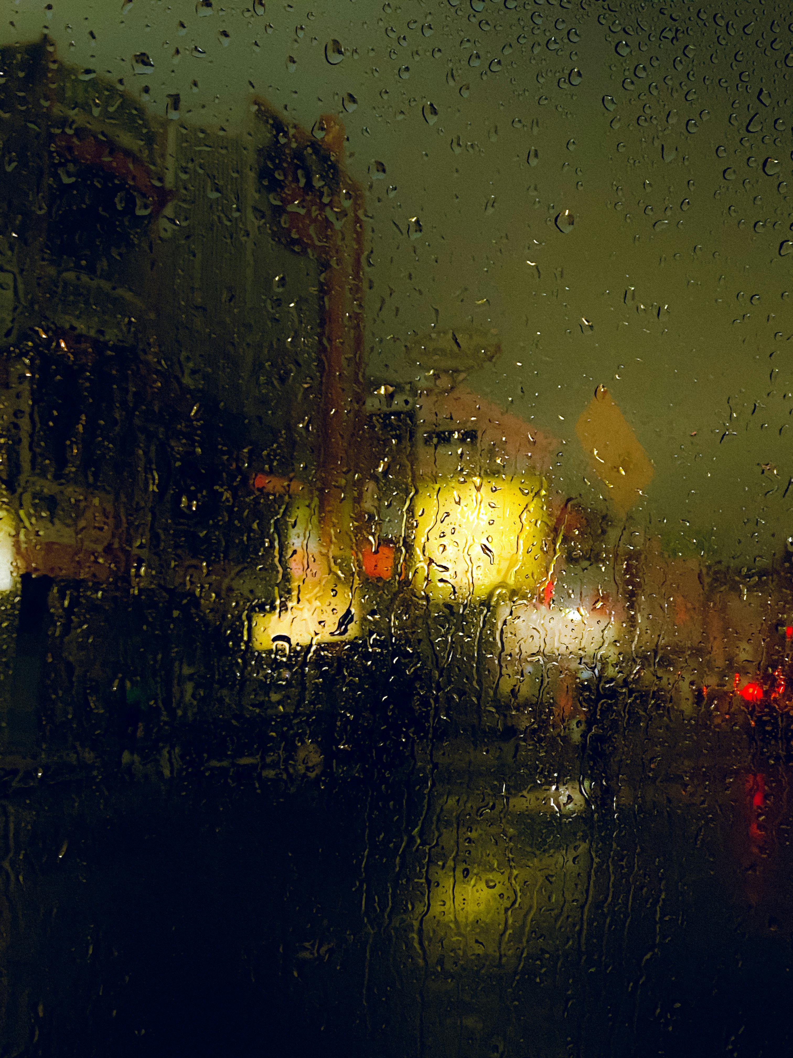 Blurry city lights seen through rain-soaked window, creating a moody urban atmosphere.