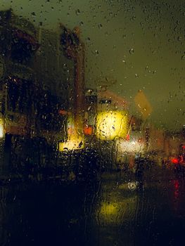 Blurry city lights seen through rain-soaked window, creating a moody urban atmosphere.