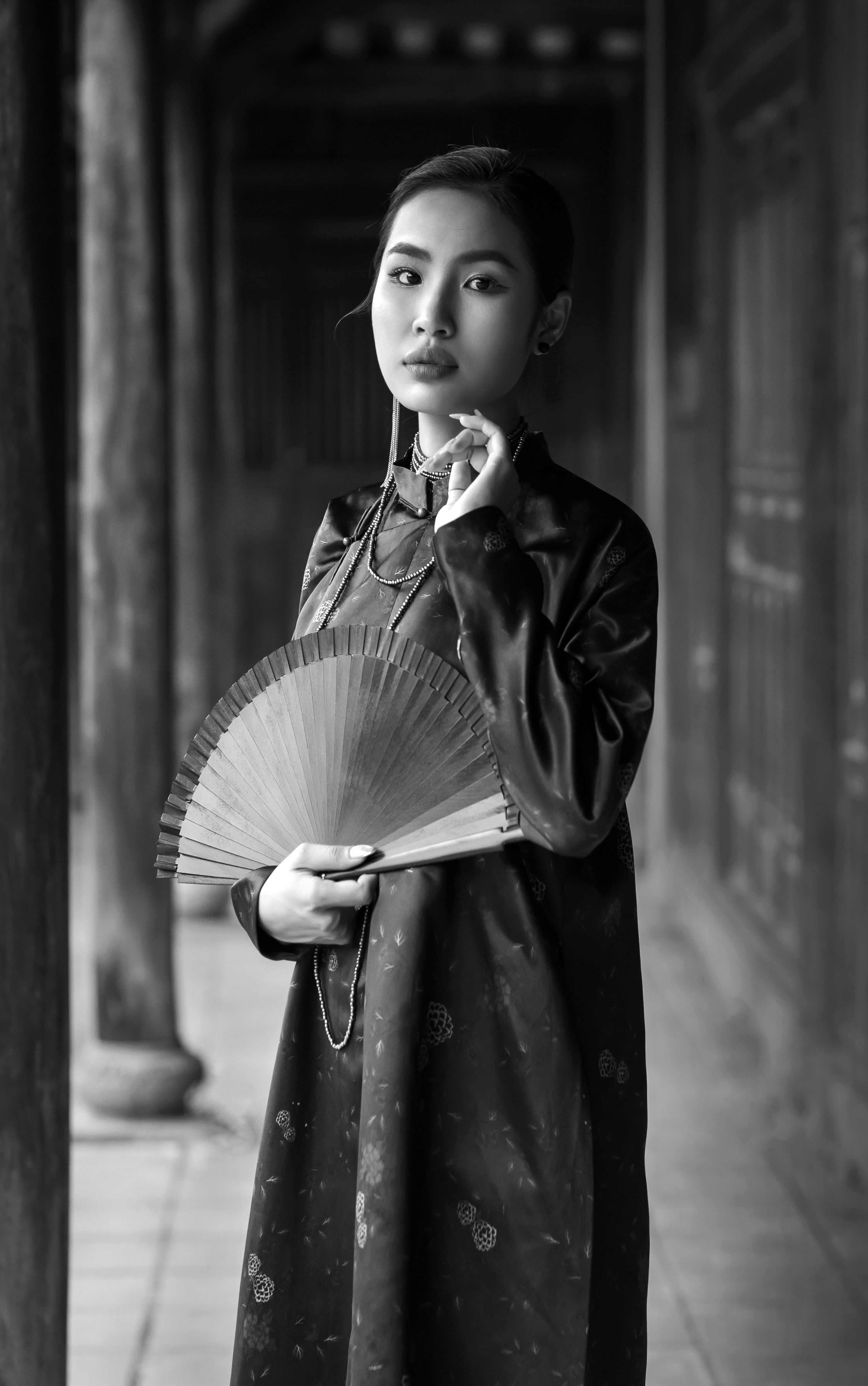 Elegant woman in traditional attire holding a fan in Hội An, Vietnam.