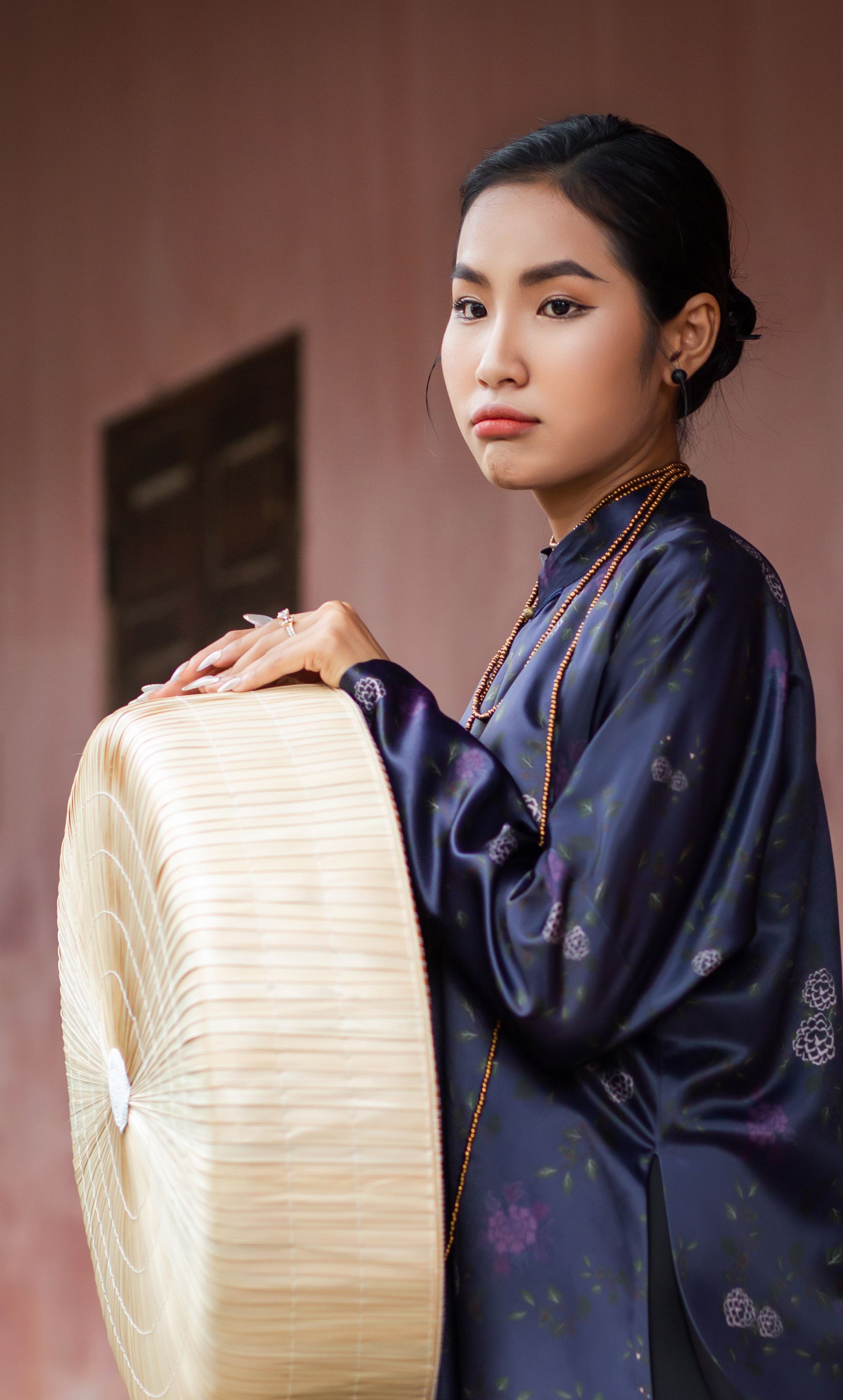 Portrait of a woman in traditional Ao Dai holding a conical hat in Hội An, Vietnam.