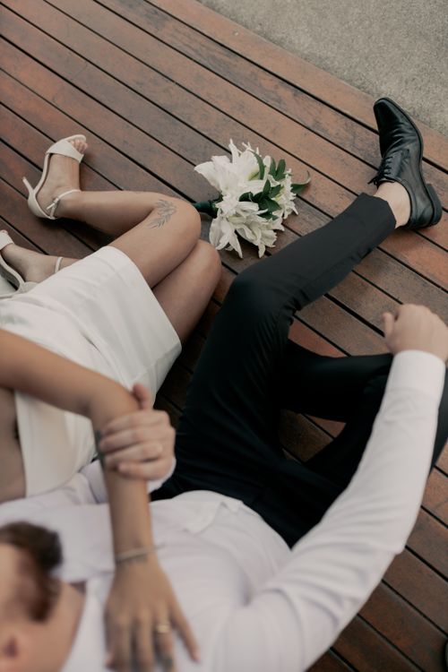 Free A couple in wedding attire resting on a wooden deck with a bouquet nearby. Stock Photo