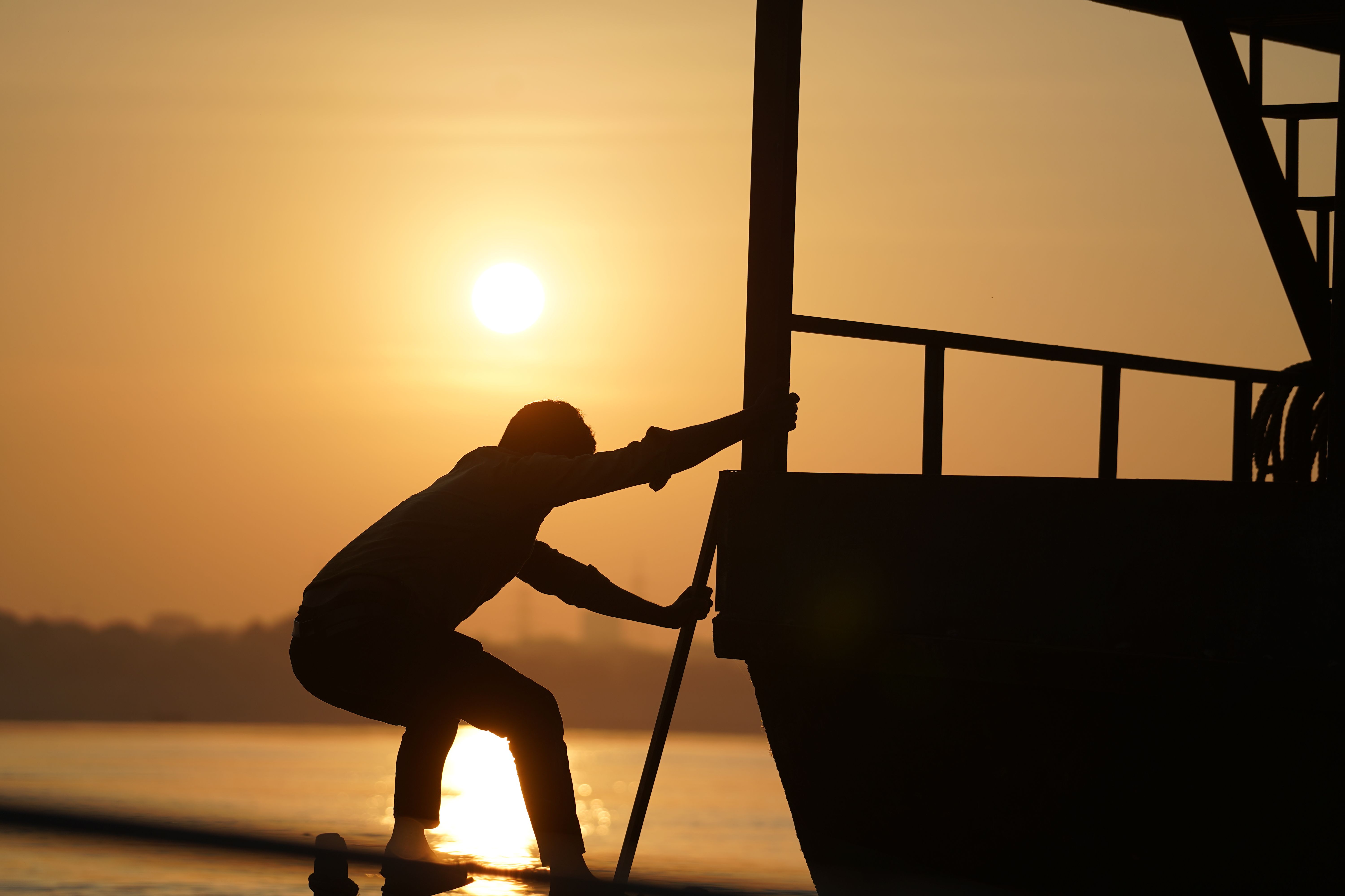 A striking silhouette of a man pulling a boat at sunrise creates a dramatic scene