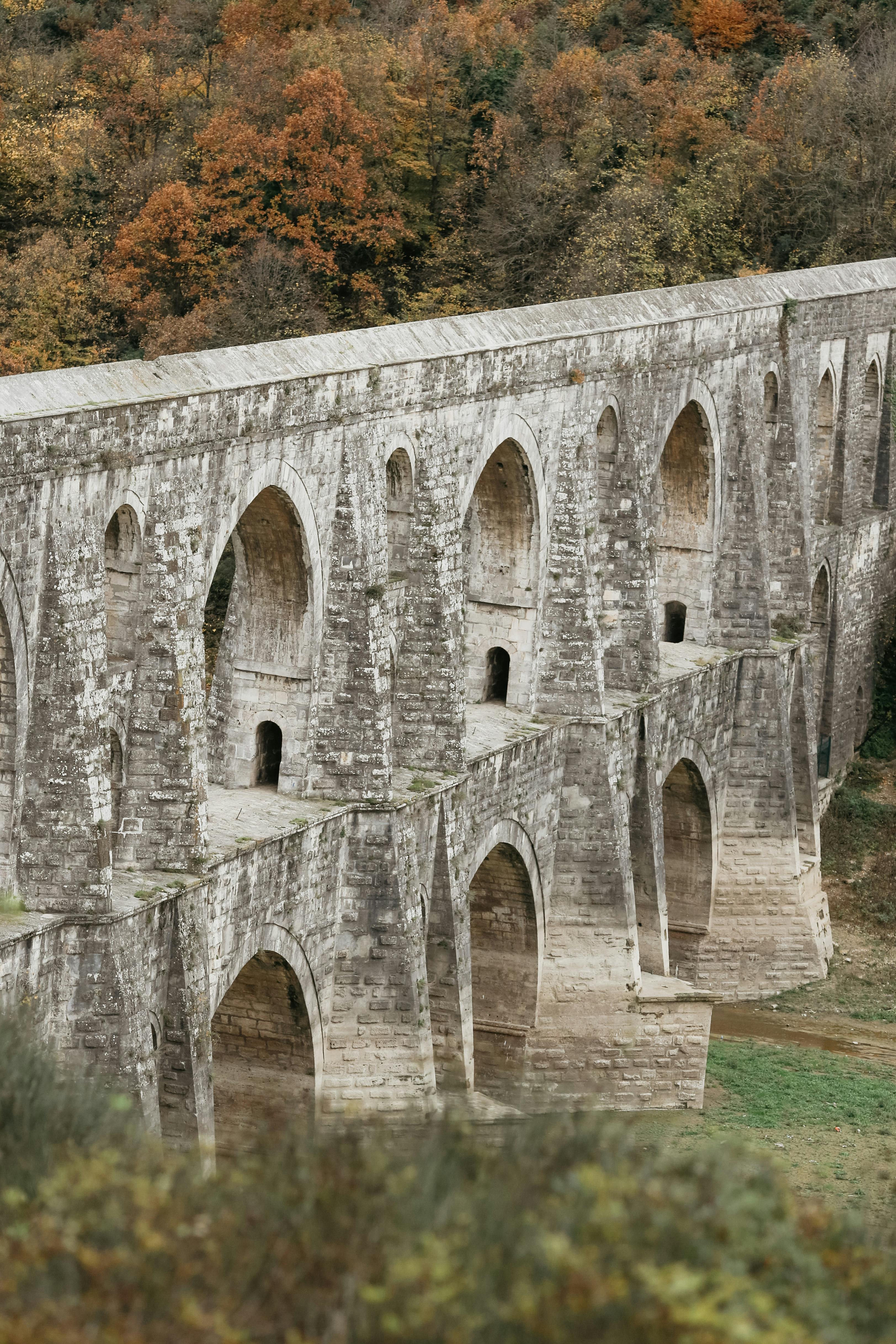 Historic stone aqueduct in Istanbul surrounded by vibrant autumn foliage, showcasing architectural grandeur.