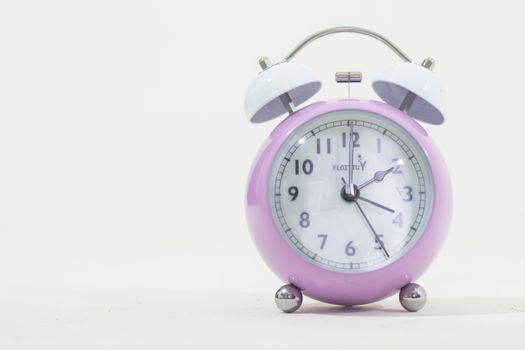 Lilac retro alarm clock with white face and bells on a plain background.