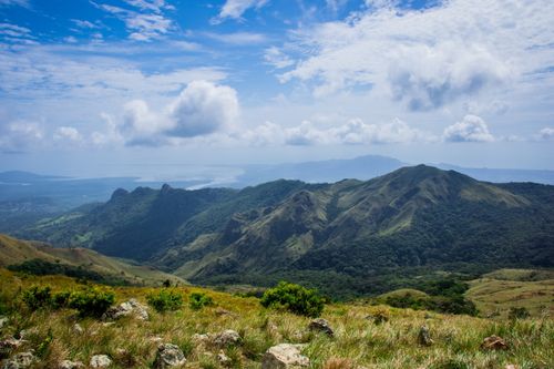Free A breathtaking view of a lush mountain range under a vibrant blue sky with fluffy clouds. Stock Photo