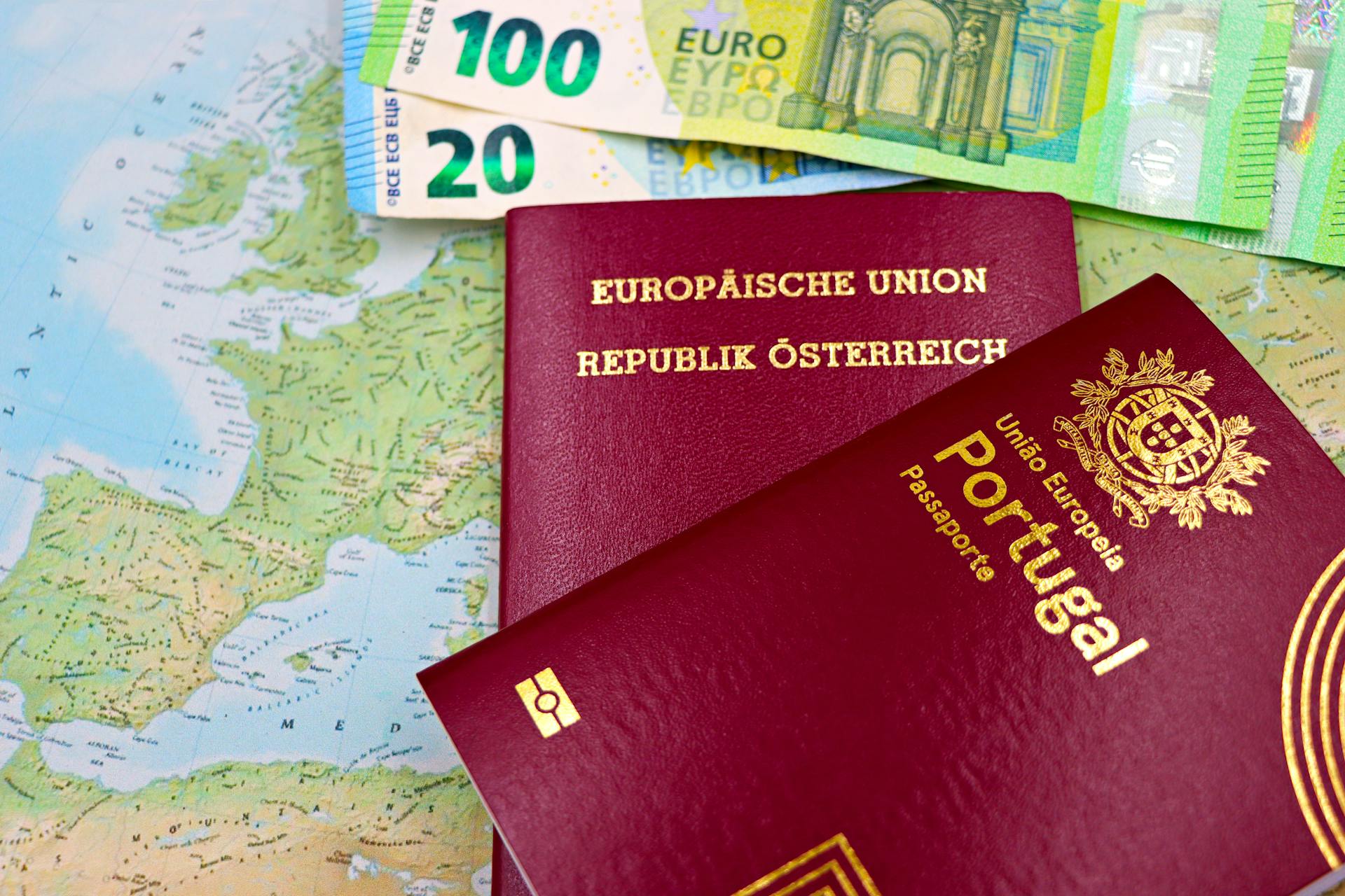 Austrian and Portuguese passports on a European map with euro banknotes.