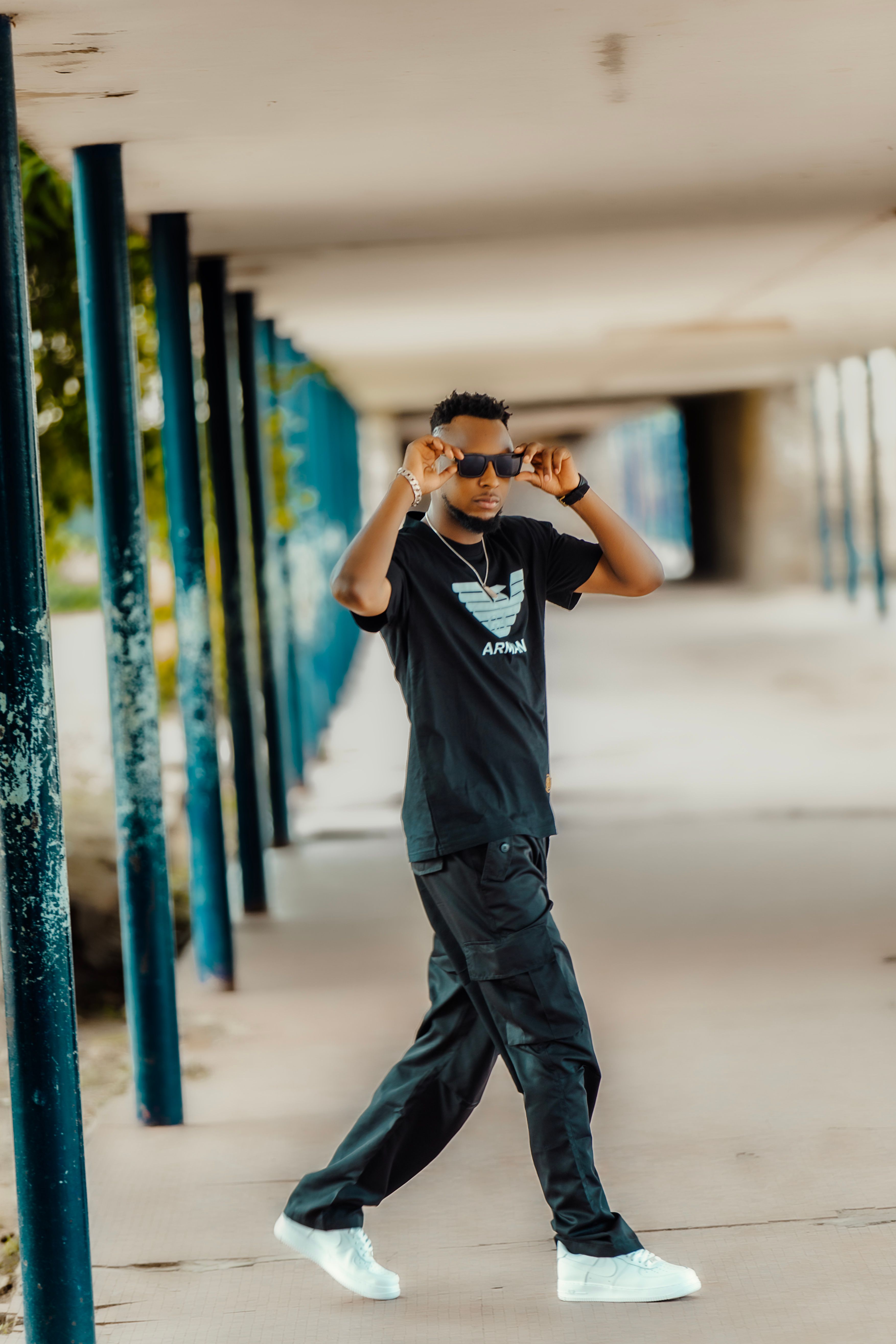 Trendy young man wearing sunglasses posing confidently in an urban corridor.