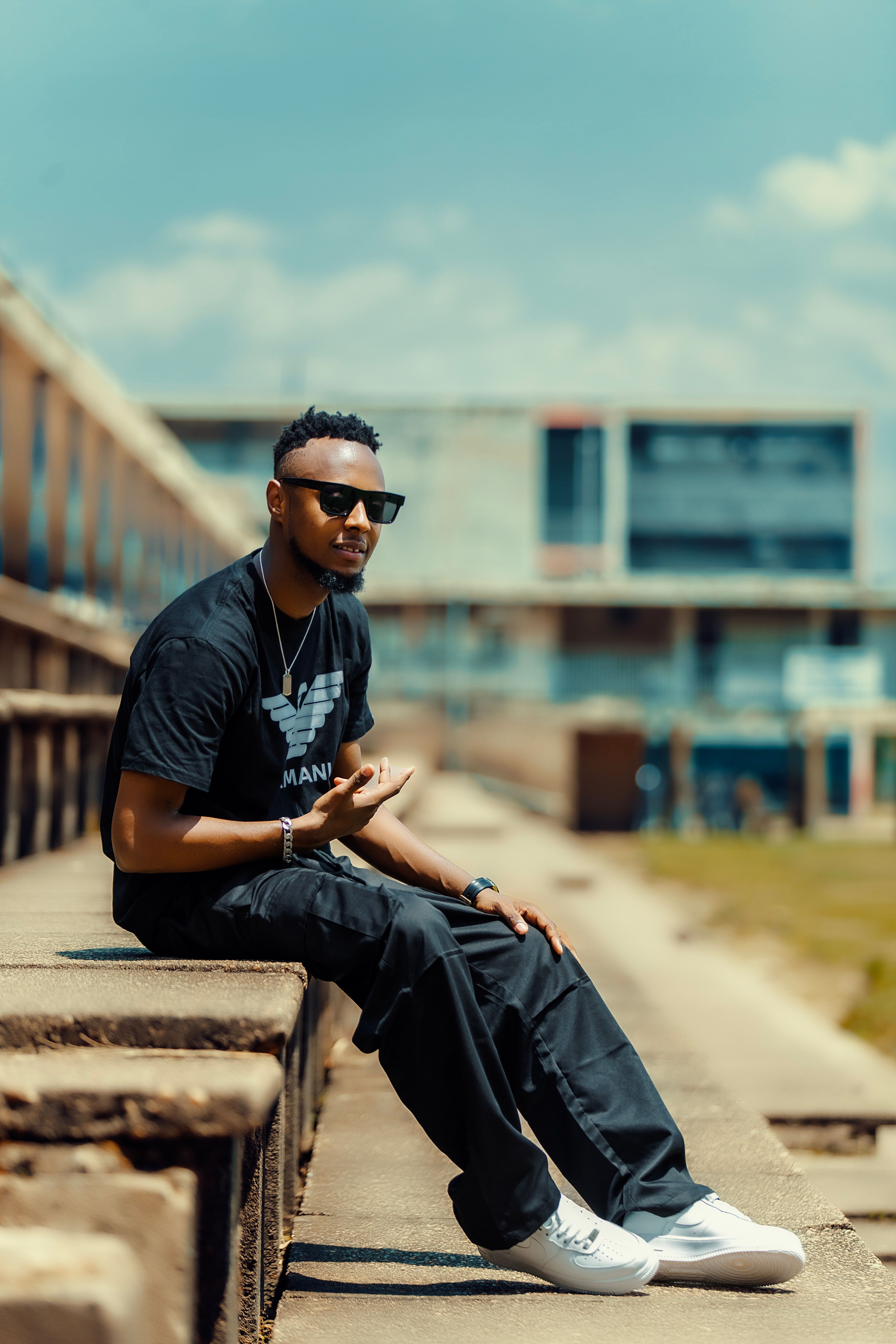 Casual urban fashion with a stylish man sitting on steps in a city setting, exuding cool confidence.