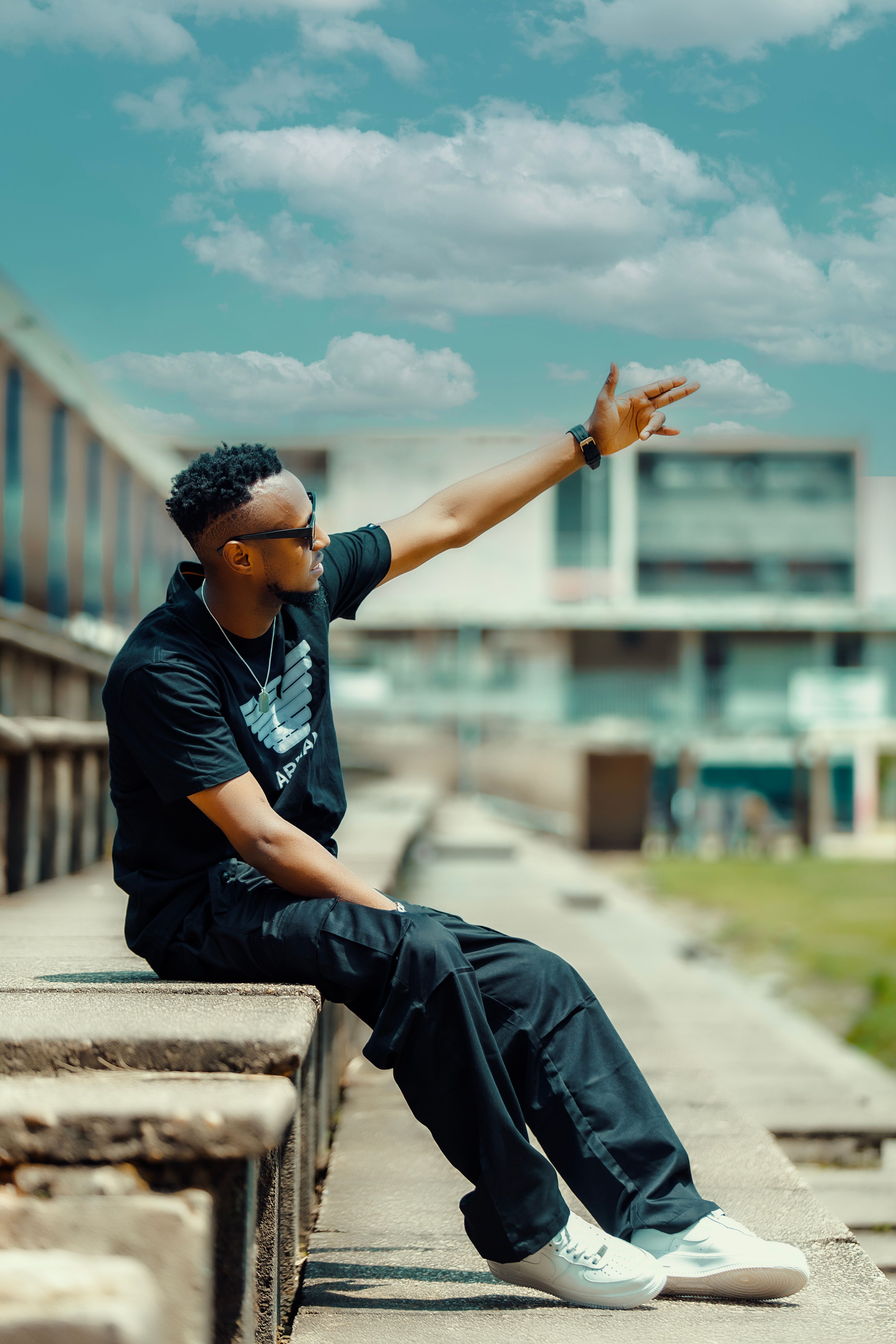 Stylish young man in casual attire gestures in a sunny urban environment.