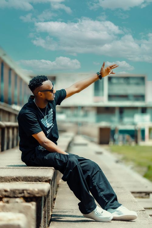 Free Stylish young man in casual attire gestures in a sunny urban environment. Stock Photo