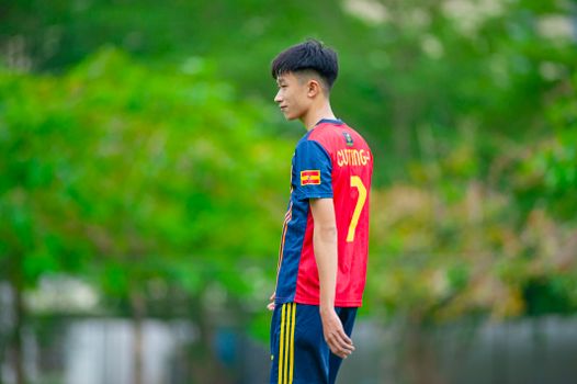 Teen soccer player wearing a team jersey standing outdoors in a lush green setting in Hanoi.