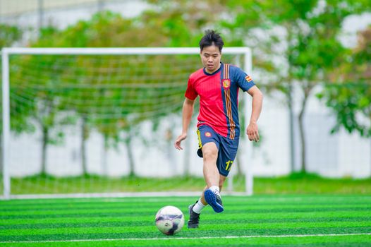 A soccer player kicking a ball on a grassy field in Hanoi, Vietnam.