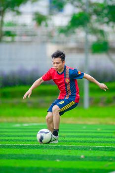 A young Asian male in a soccer jersey playing on a green field in Hanoi, Vietnam.