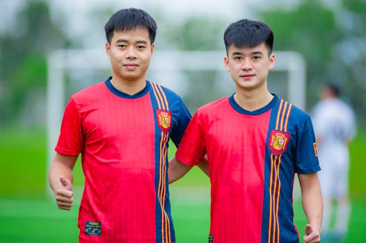 Two young men in soccer uniforms posing on a green field in Hà Nội, Việt Nam.