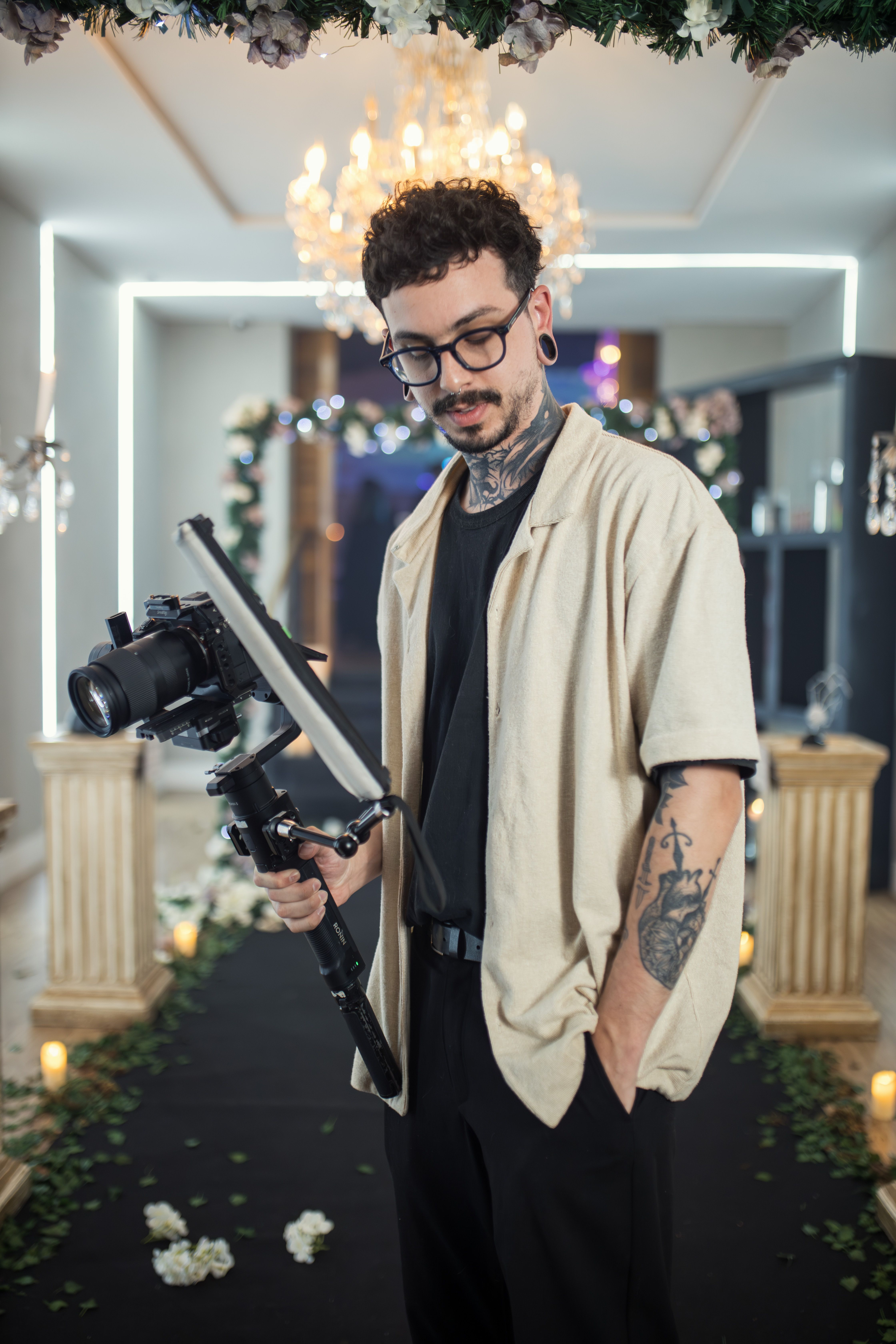Tattooed male photographer with gimbal, capturing an indoor event with elegant decor.