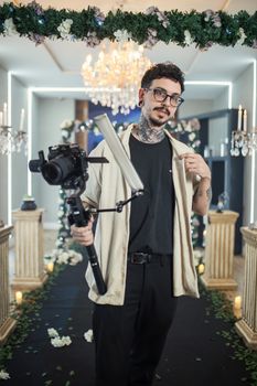 Photographer holding camera gear at upscale, indoor wedding event.