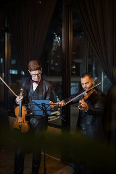 Two violinists performing a duet in an elegant indoor setting. Nighttime ambiance.