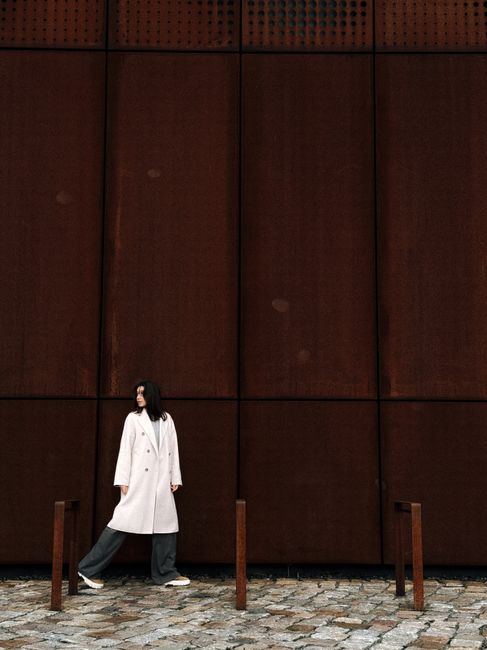 A fashionable woman poses against a rust-colored wall in Dresden, Germany.