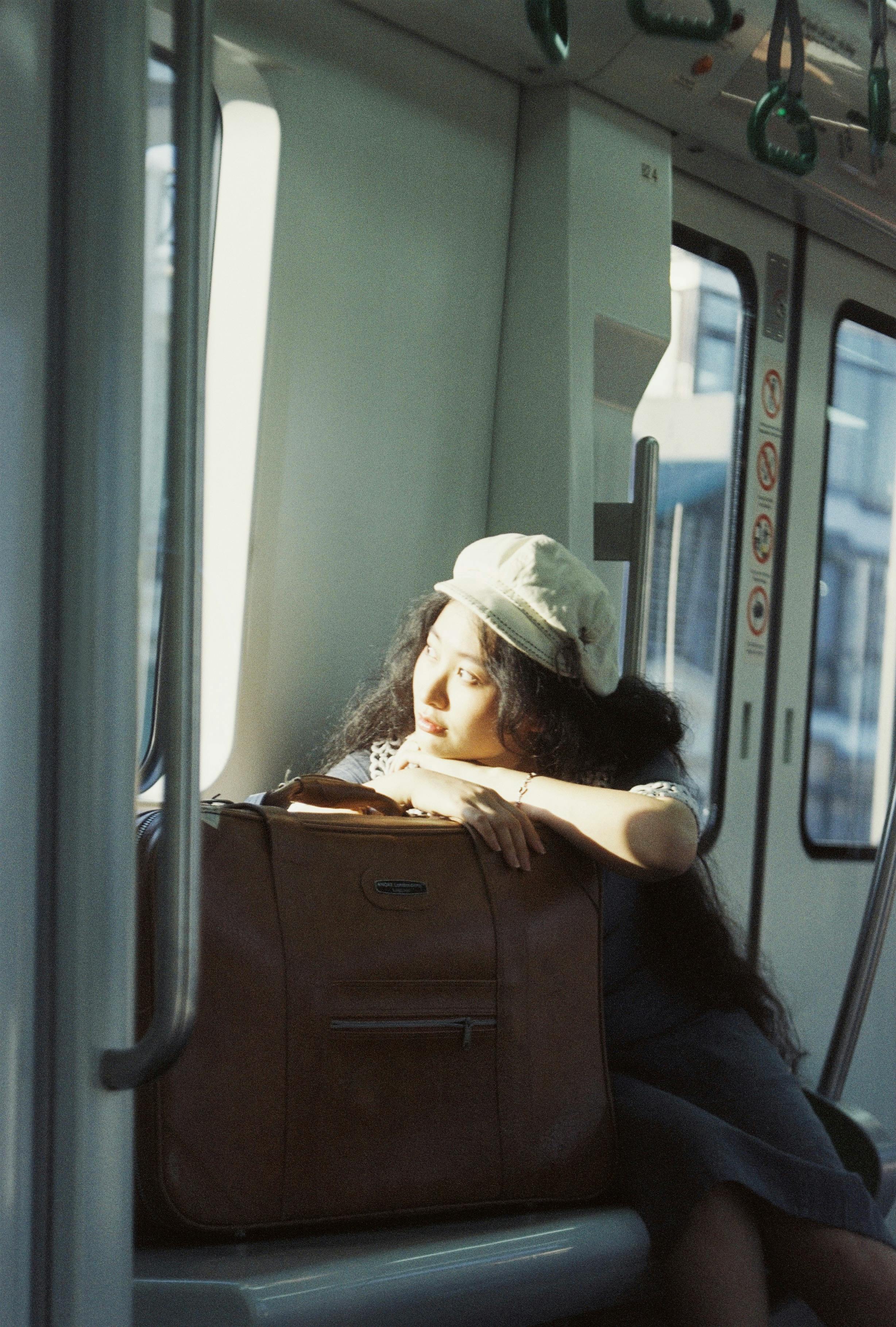 A thoughtful woman gazes out train window, sunlight casting a warm glow.